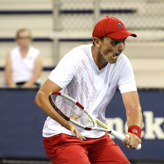 a man is wearing red pants, a white t - shirt and a red hat playing tennis