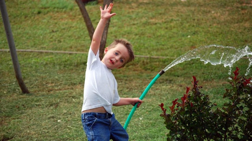 a child holding onto an open green hose to cool water