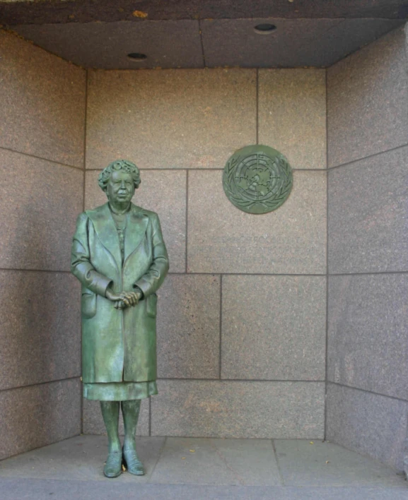 statue of woman wearing long green coat near gray stone wall