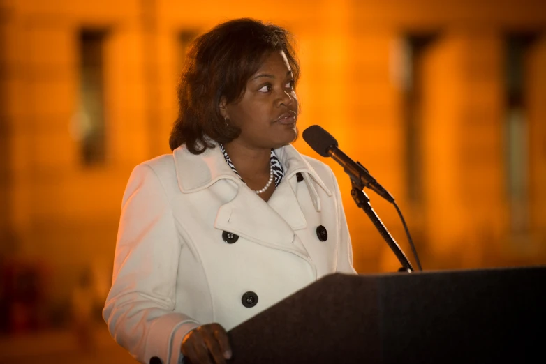 woman speaking into a microphone with a long jacket over her shoulders