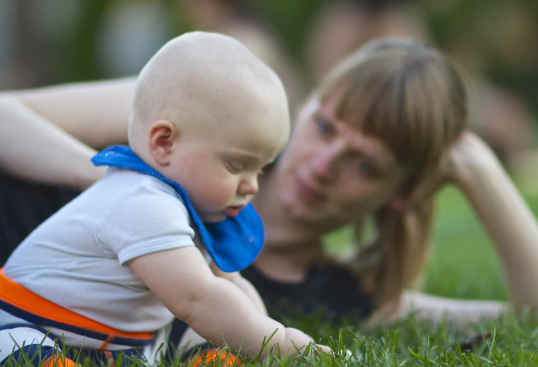 a woman laying in the grass next to a baby on it's back