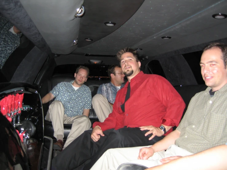 four guys sitting in the back of a car and some wearing suits