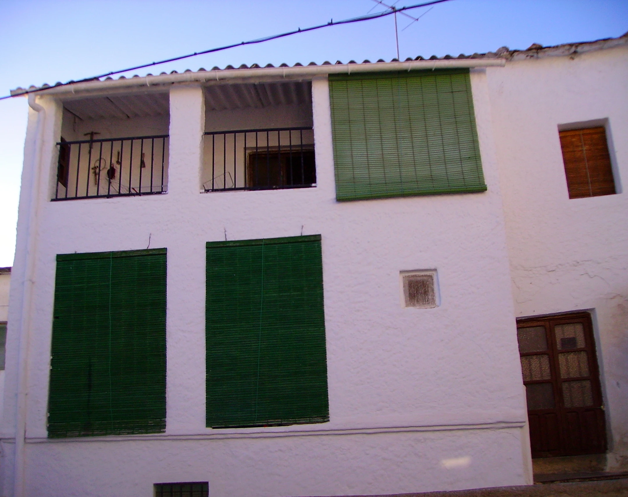 the front facade of an old building with shutters and green doors