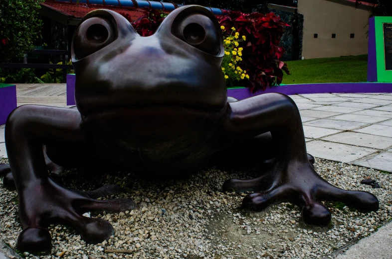 a large frog statue sitting in front of some flowers