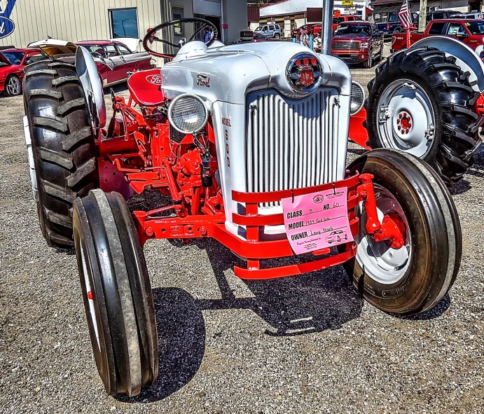 an antique red tractor is displayed with other antique tractor parts in the background