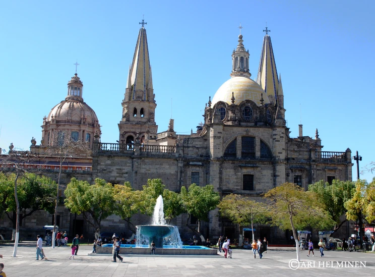 a city square with people walking around and the buildings of a church