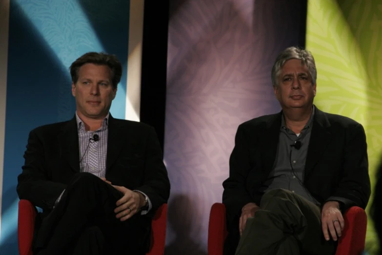 two men sitting in chairs and one holding a wii controller