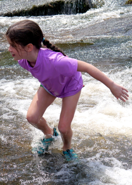 girl in purple shirt wading through a stream