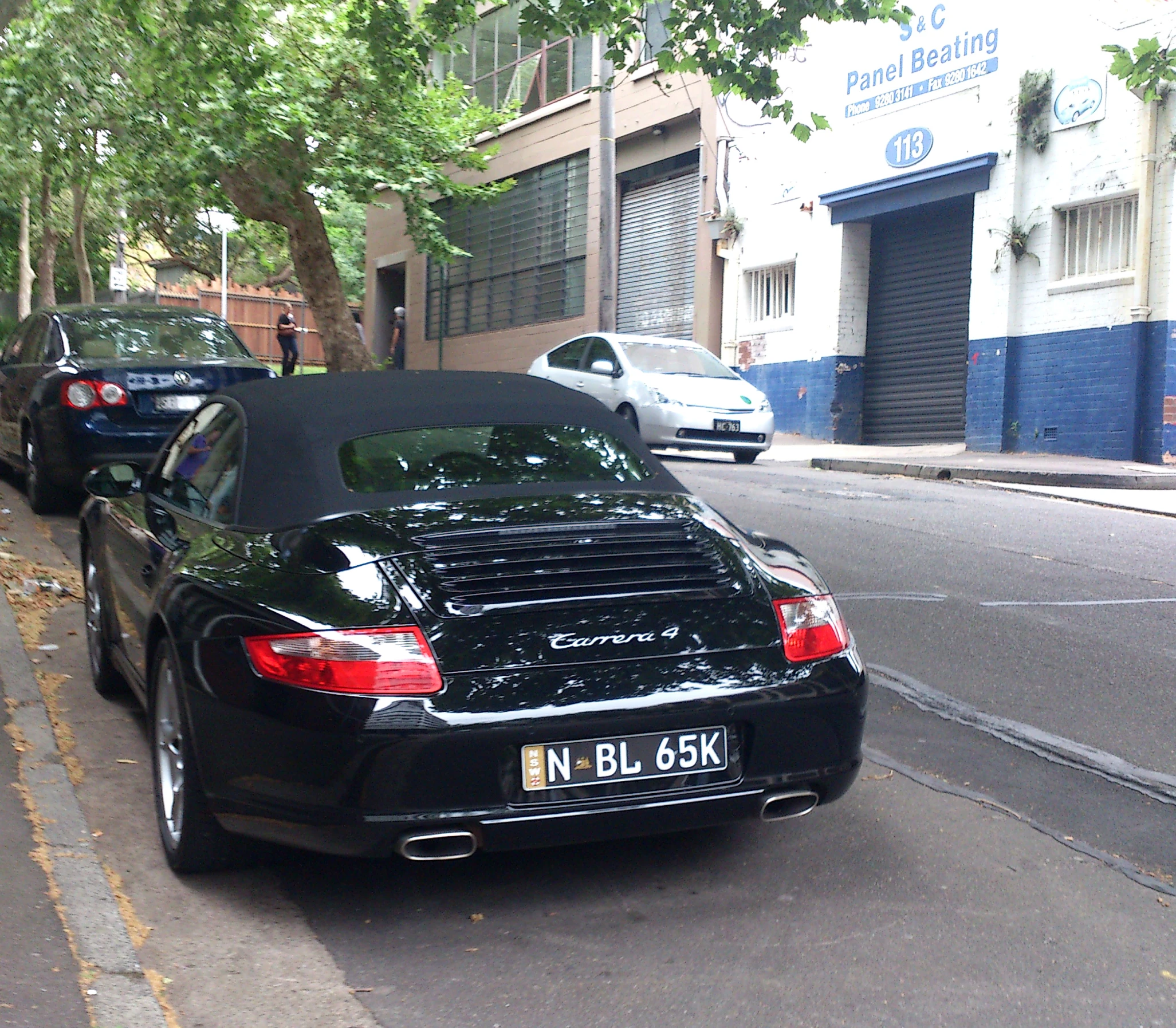 the back view of two black cars parked on the side of a road