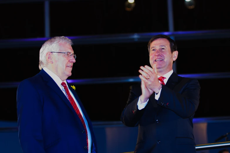 two men in suits applauding each other while on stage