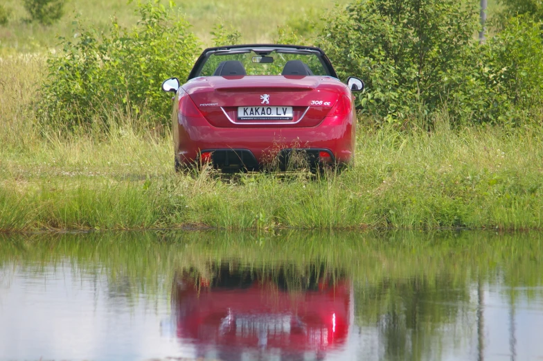 a small red convertible car in the grass near water