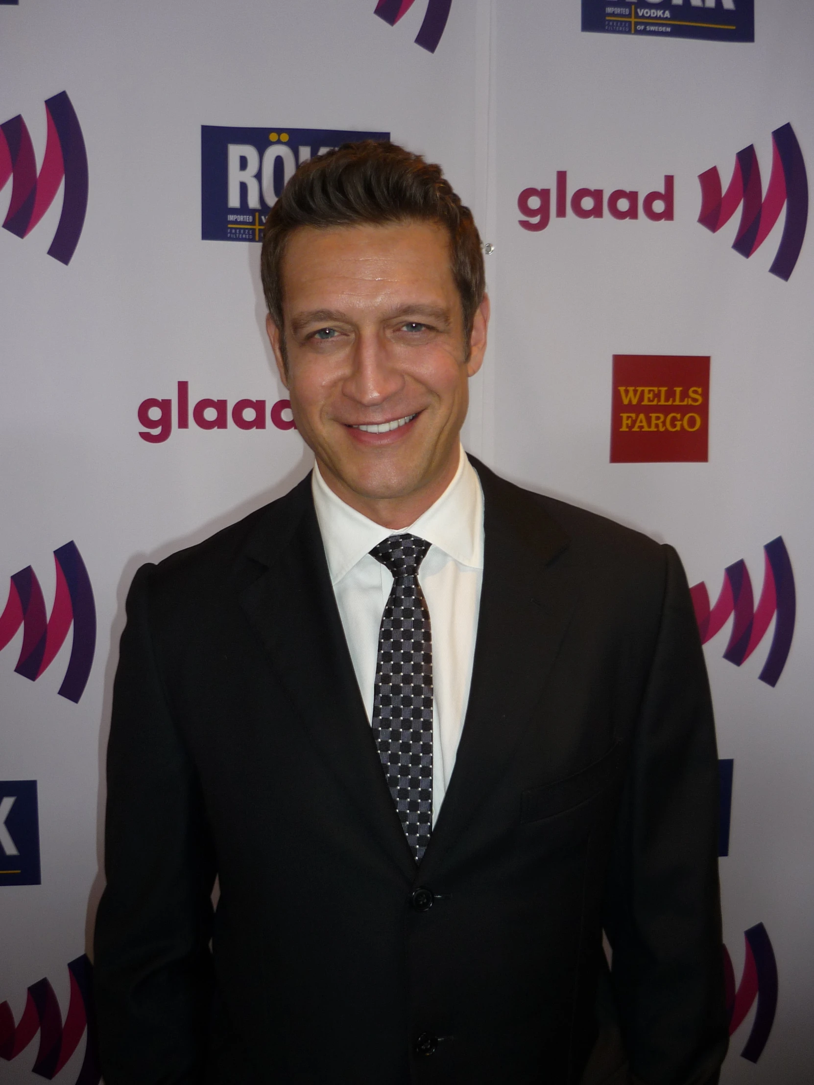 a smiling man in a black suit and tie