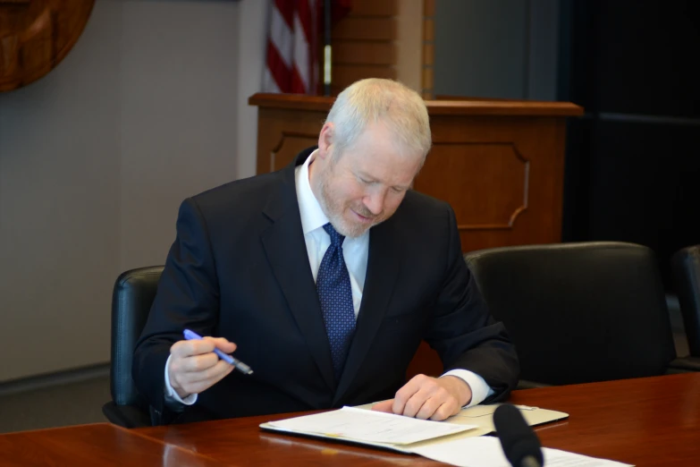 a man in suit signing a paper at a desk