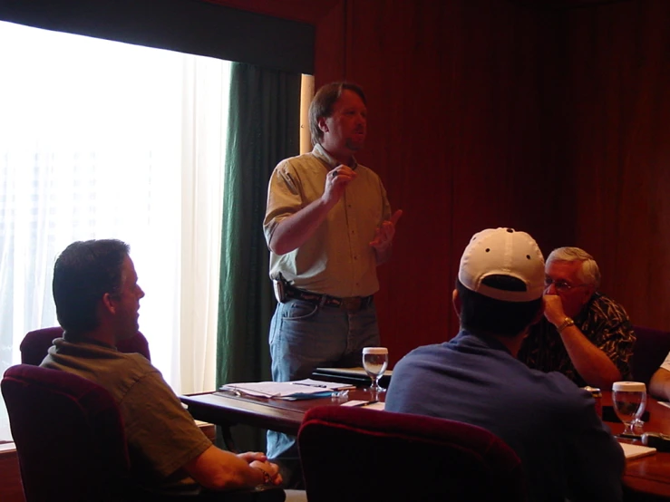 a man in white helmet and other people seated around a table