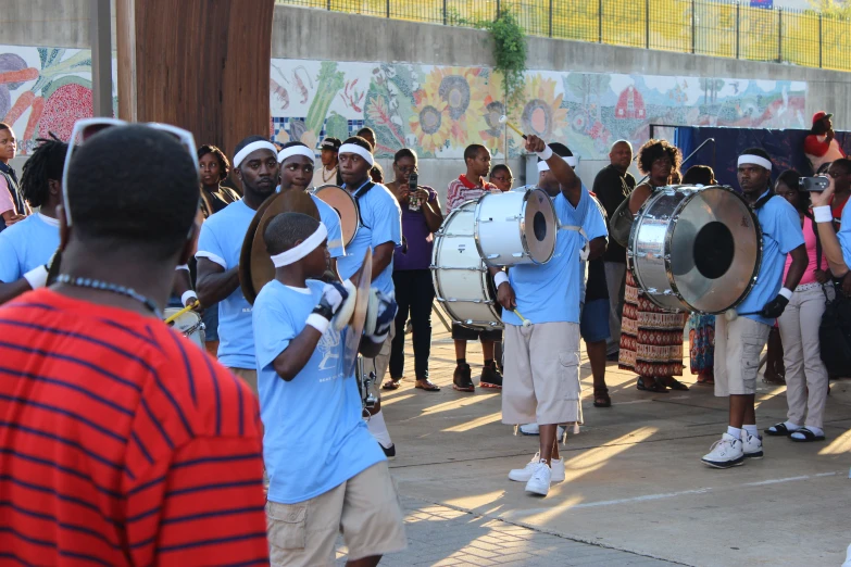 an ensemble of men in blue outfits playing drums on a street