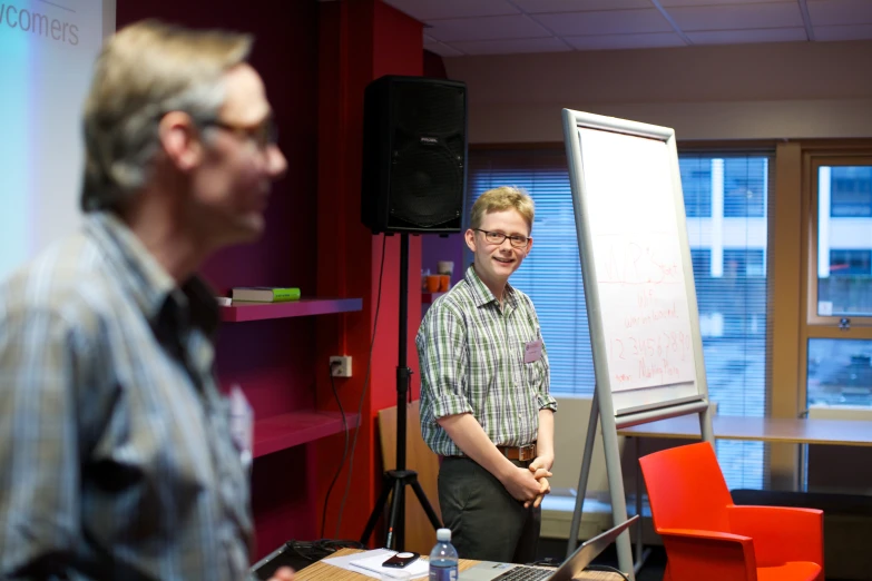 two men stand next to a dry erase board