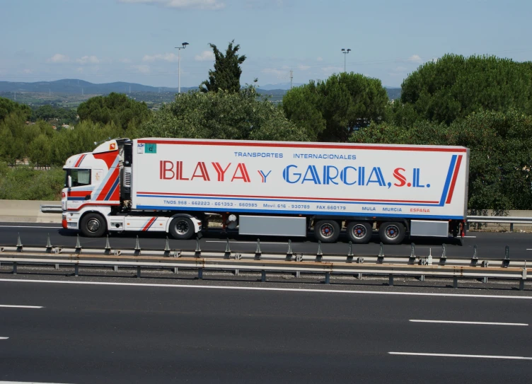 a semi trailer truck on a highway with trees in the background