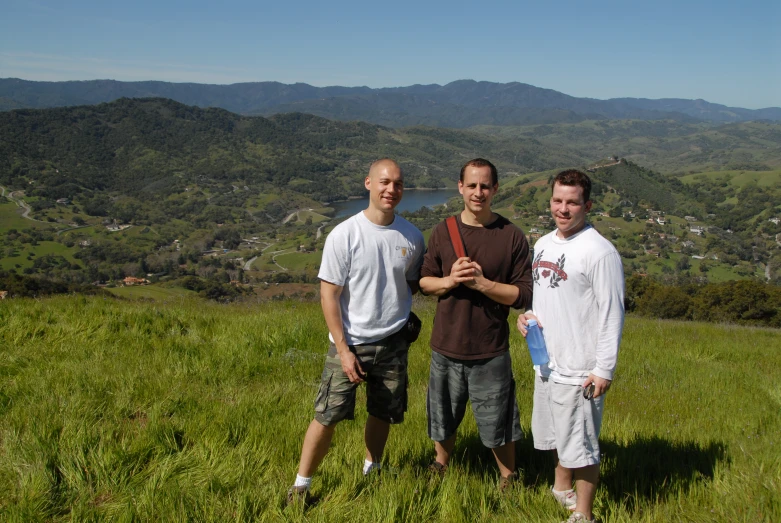 three men are standing in the grass near mountains