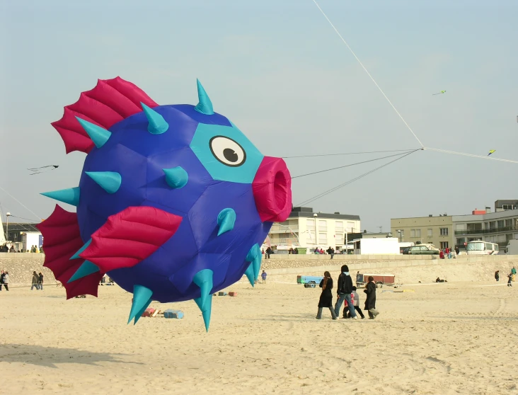 people flying a kite in the sand with a giant blue and red fish balloon on the beach