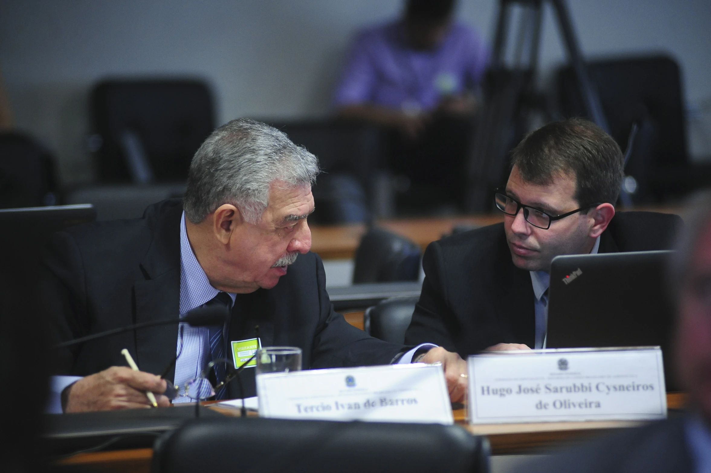 two men are in business suits sitting at a table looking at their laptops