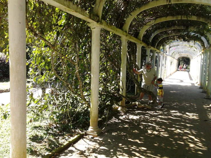 a man and small boy are standing under an arbor in a green garden