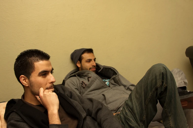 a man sitting next to another man on the bed
