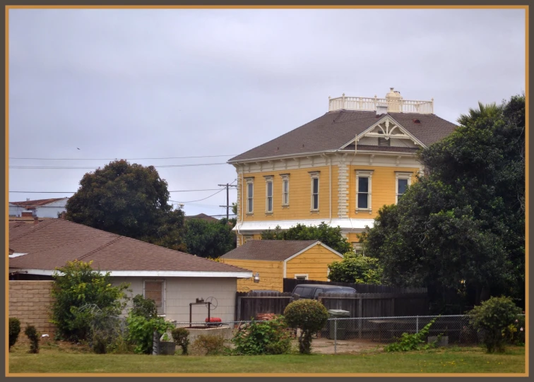 a yellow house is behind some green bushes