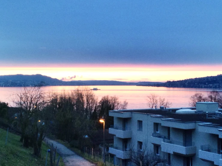 the sun is setting near a building overlooking a lake