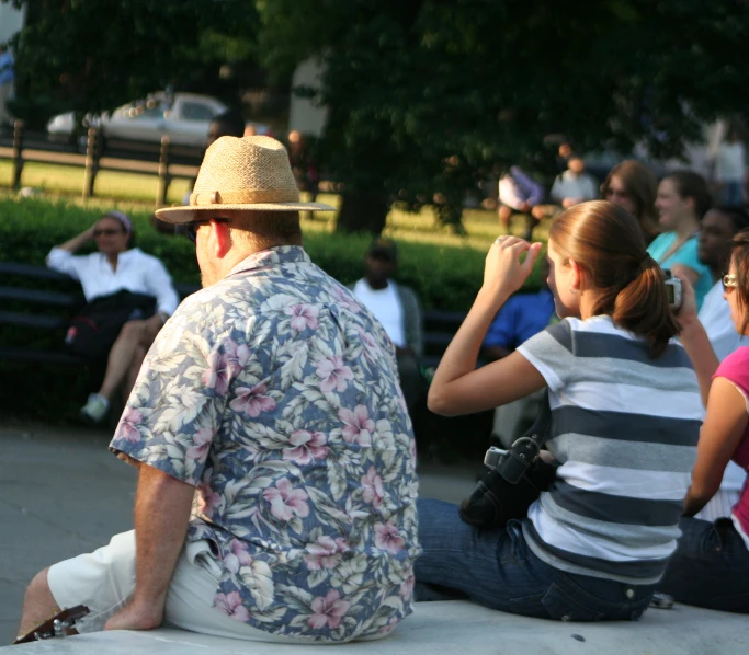 a man in a floral shirt sitting down while his friends take pos