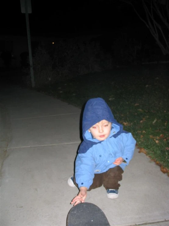 a  wearing a blue coat with white shoes sits on a skateboard in front of the sidewalk