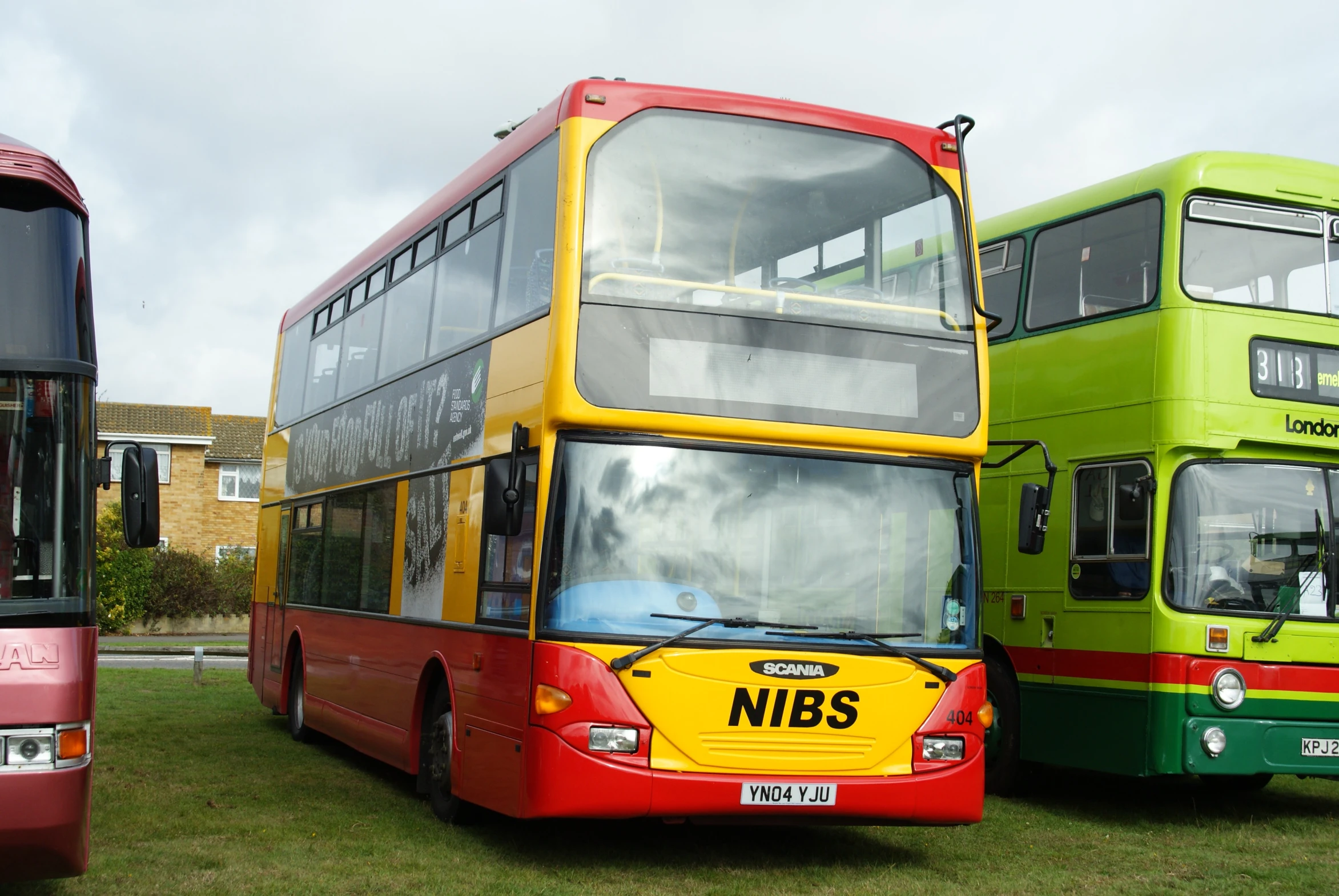 three different colored double decker buses parked on grass