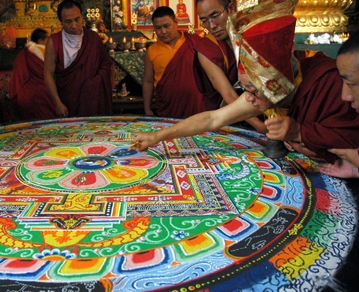 buddhist monks stand around a multi - colored psychedelicly painted cloth