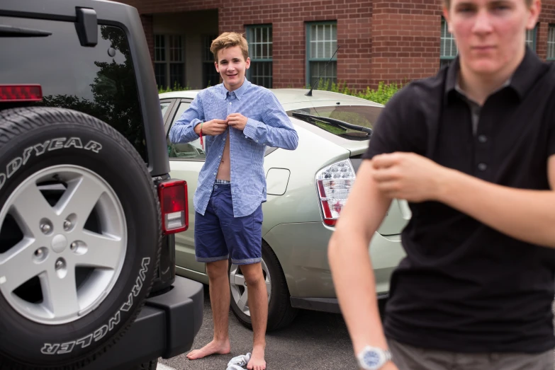 two boys with open shorts by some parked vehicles