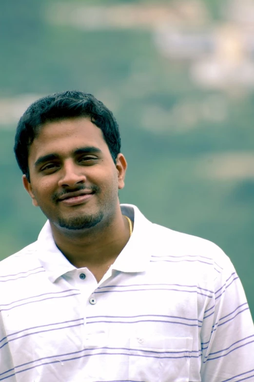 an indian man with a smile standing by a cliff