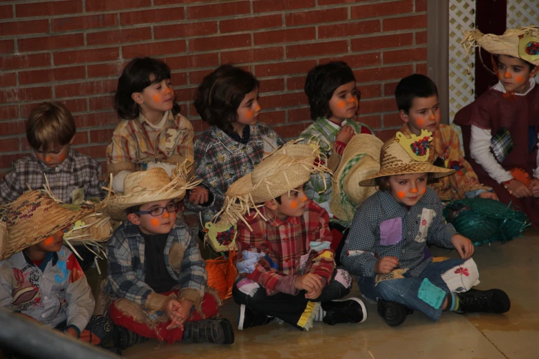 young children dressed up as scarecrows and children with face paint sit on the ground