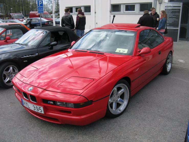 a red bmw z3 sits parked in front of a line of parked cars