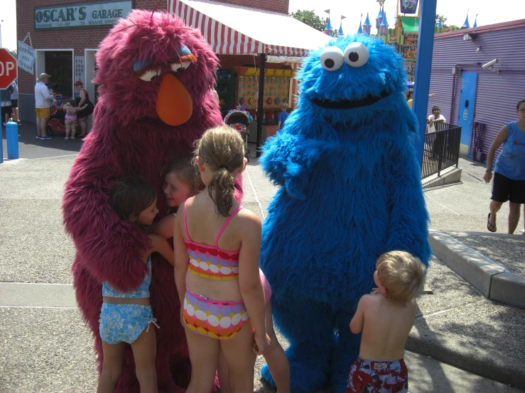 two adults, one child, and a baby standing beside a sesame street character