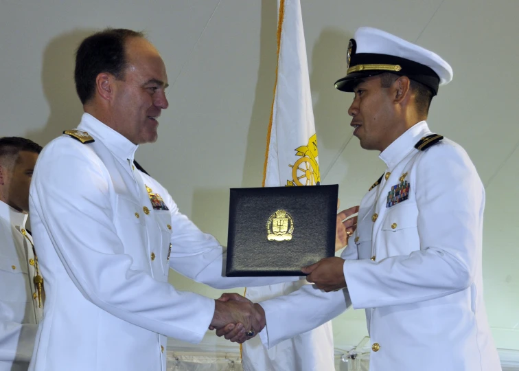 two military men shake hands over a plaque