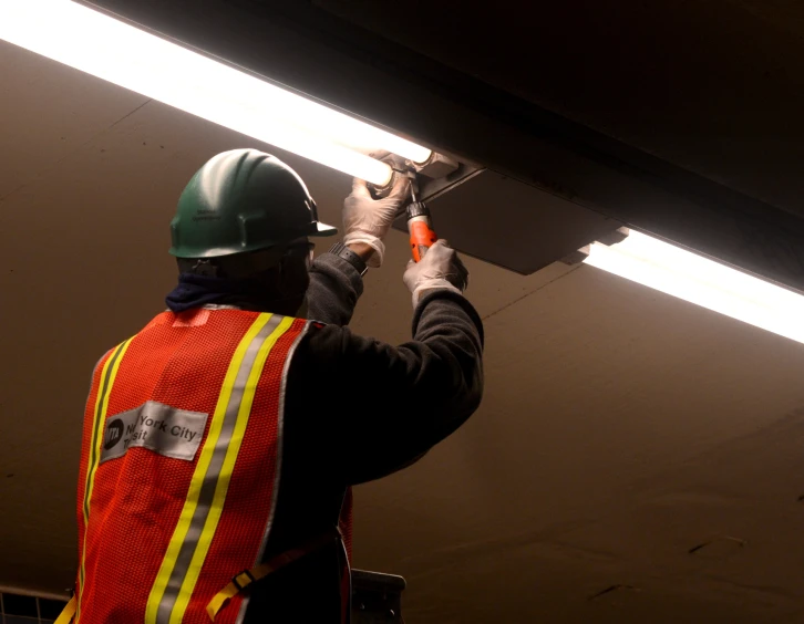 an industrial worker adjusts a fluorescent strip light in the hallway