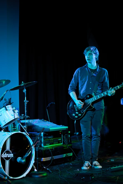 a male with a guitar and drums playing in front of some drum set