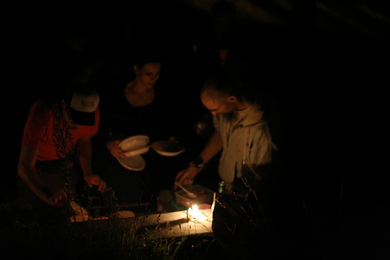 three people outside in the dark preparing food