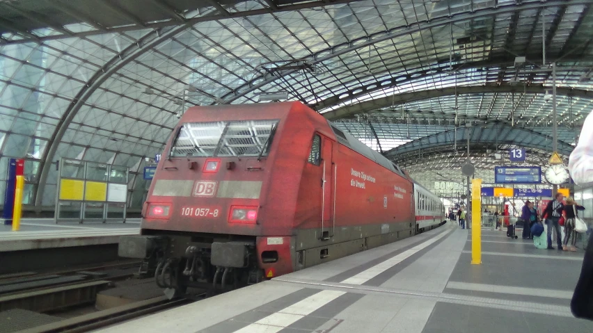 a red train parked at an empty platform with people walking by