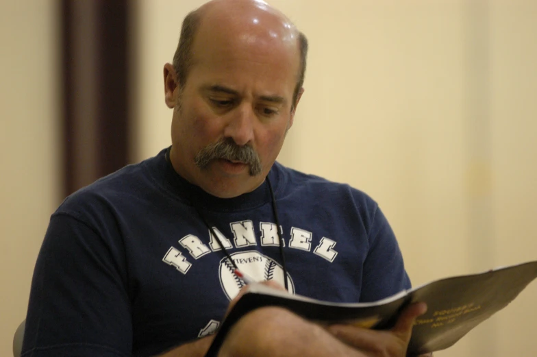 a bald man wearing a baseball uniform reading from a book