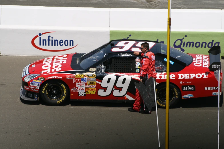 a red car sitting in a parking lot next to a giant flag