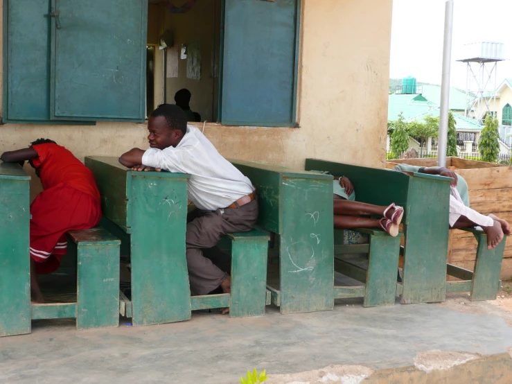 two men sleeping in front of an entrance with a red woman lying on the bench