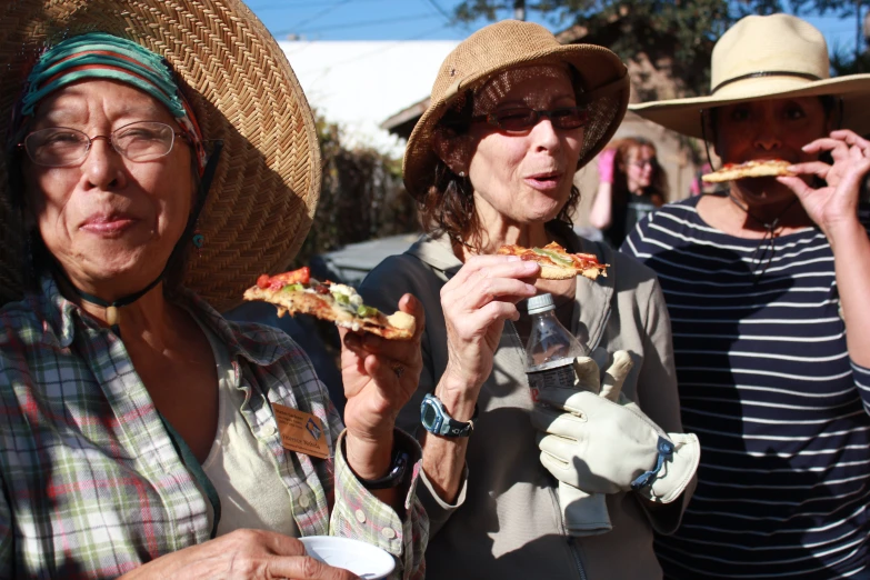two women wearing hats and eating pizza