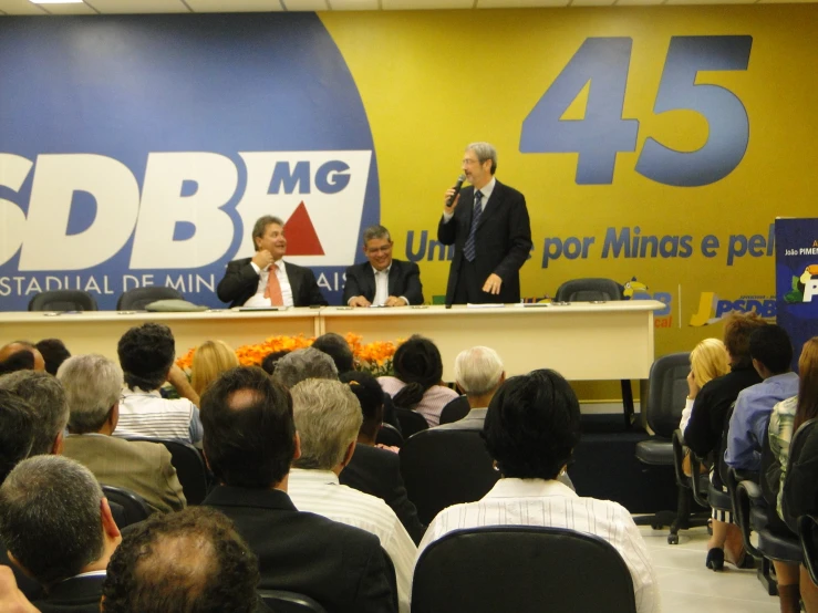 two men and woman at the podium with an audience