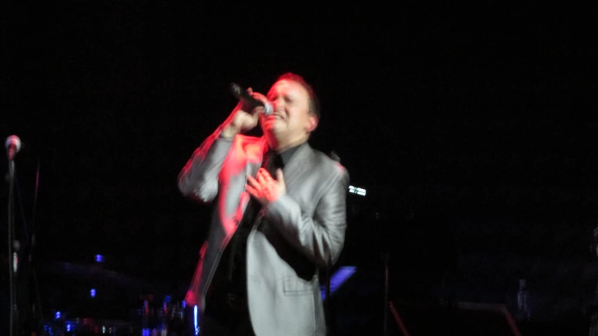 the man is singing into a microphone while wearing a suit