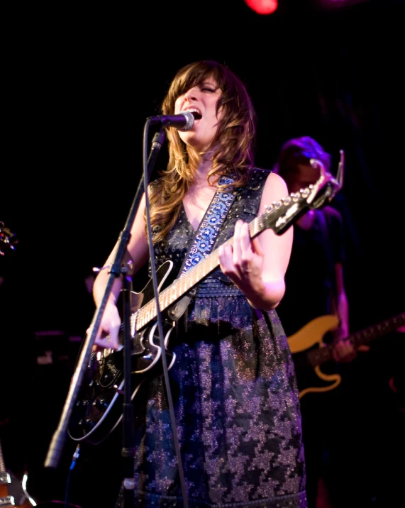 a woman sings into a microphone while holding an electric guitar