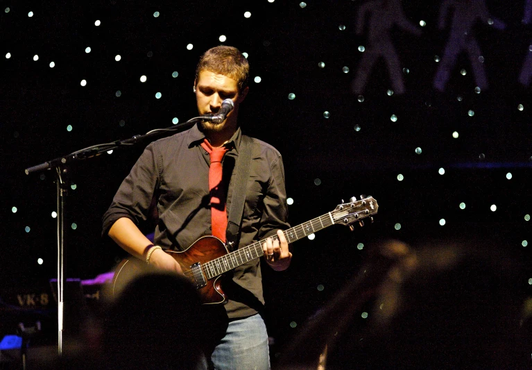 a man with a guitar sings into microphones